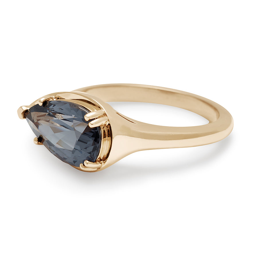 Angled view of a solitaire ring pear shaped grey spinel set in yellow gold.