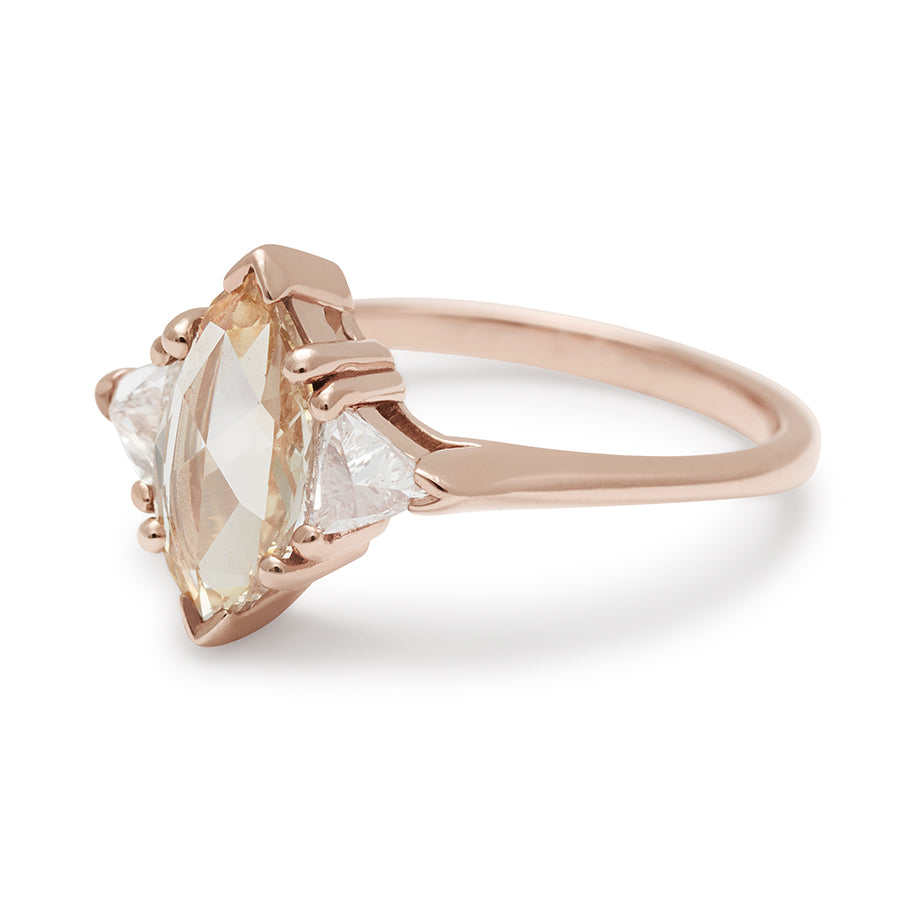 Angled view of a three stone engagement ring with a marquise shape 0.85ct champagne diamond center stone with two white diamond trillion side stones set in rose gold.