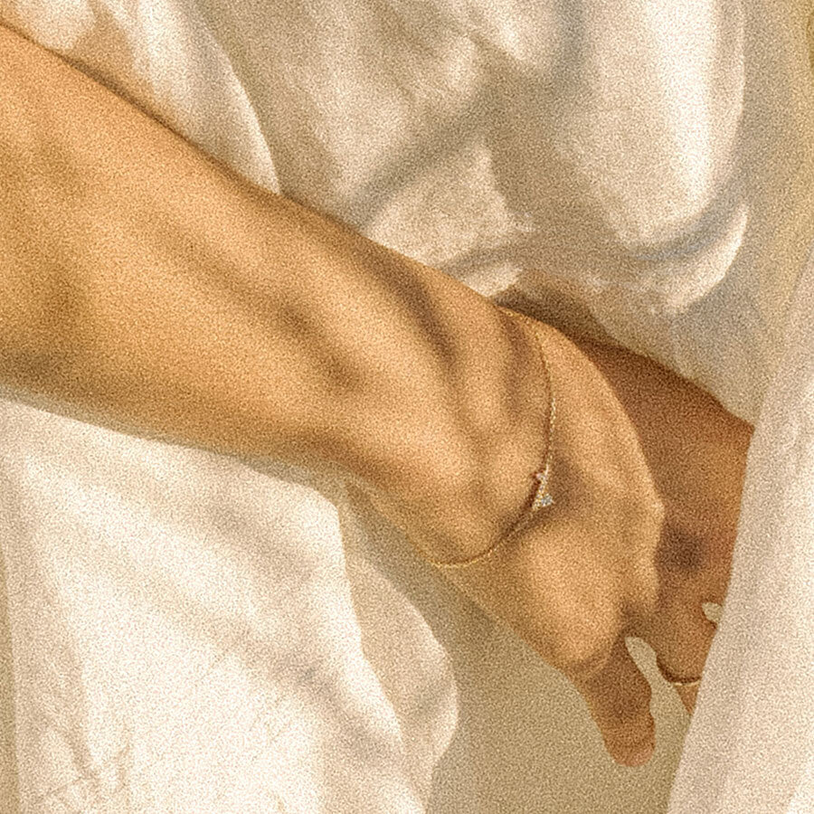 A straight line of white diamond pave with grey and black diamond accent stones on either side set in a yellow gold chain bracelet on a light-complexion wrist.