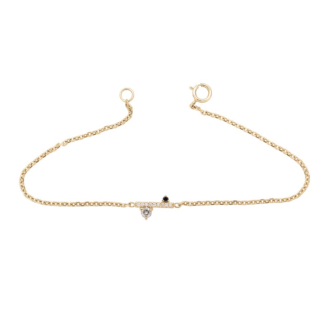 A straight line of white diamond pave with grey and black diamond accent stones on either side set in a yellow gold chain bracelet.