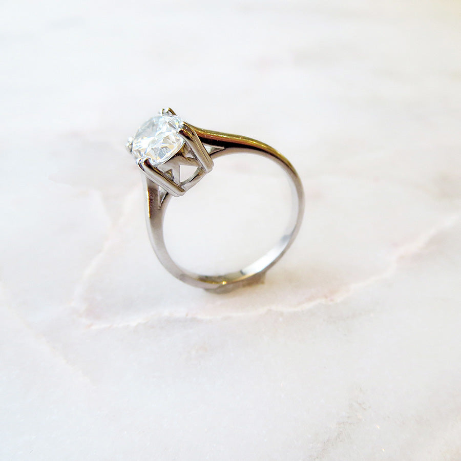 Angled view of a solitaire ring oval white diamond set in white gold on a circular blue stone.