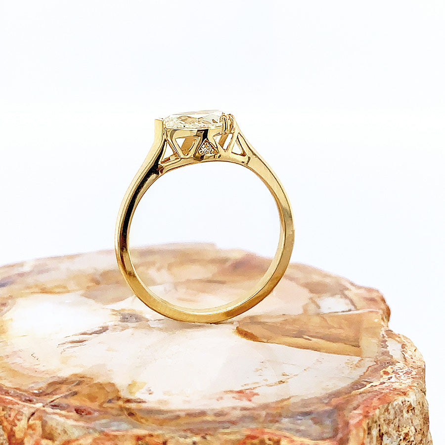 A side view of a pear shaped ring with a white diamond stone set in yellow gold and placed on a piece of wood.