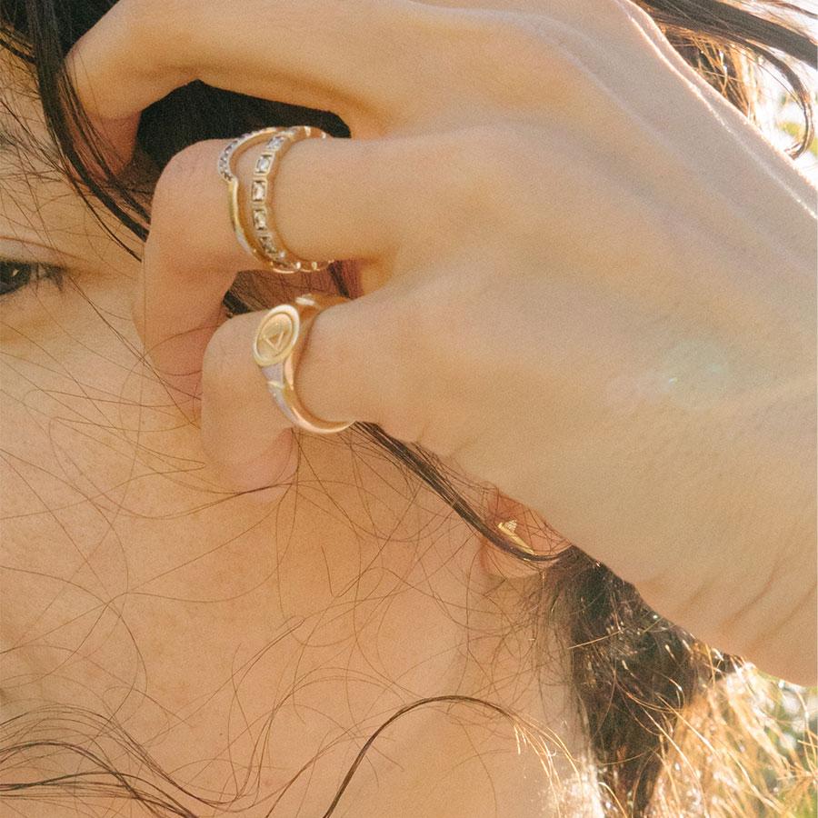 A solid gold signet ring with two white diamond accents on either side and set in yellow gold on a medium-complextion pinky ring with two diamond accent band on her ring finger.