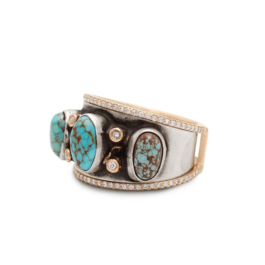 Angled view of a one of a kind turquoise stone band with white diamond accent stones set in sterling silver with a double banded accent band set around with white diamond pave and yellow gold.