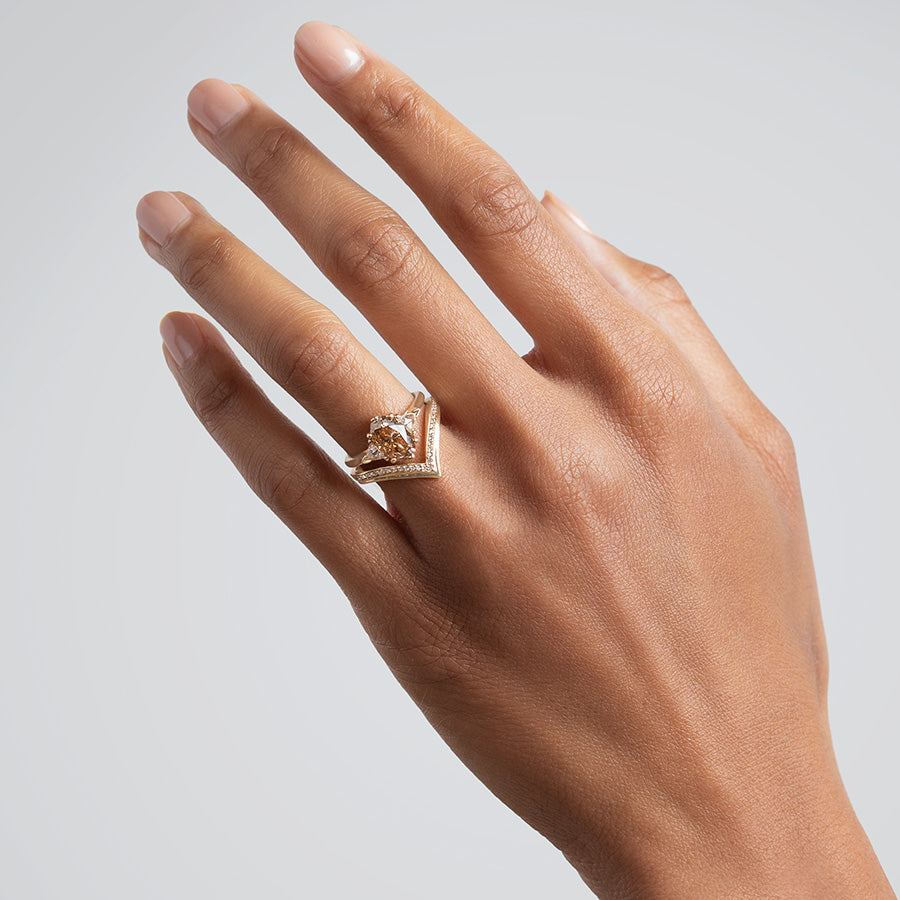 A three stone engagement ring with an oval shape champagne diamond center stone with two white diamond trillion side stones set in yellow gold above a chrysalis band with white diamonds set in yellow gold on a medium-complexion model. Available in White Gold, Yellow Gold, Rose Gold.