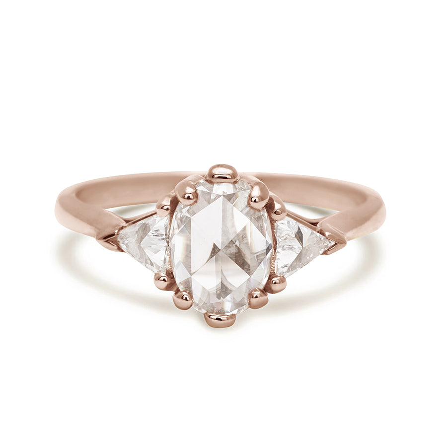 A three stone engagement ring with an opal shape white diamond center stone with two white diamond trillion side stones set in rose gold.