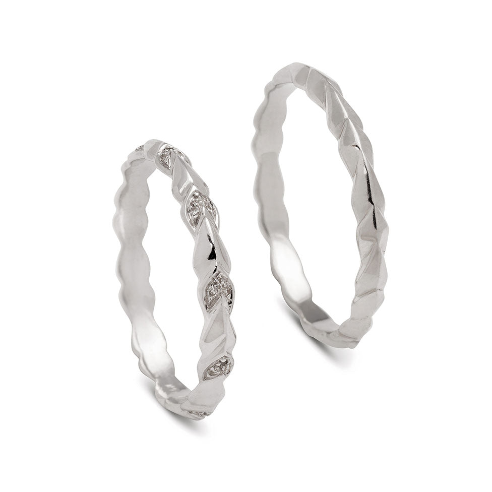 A straight band with leaf like definition with white diamond accents set in white gold next to a straight band with leaf like definition set in white gold.