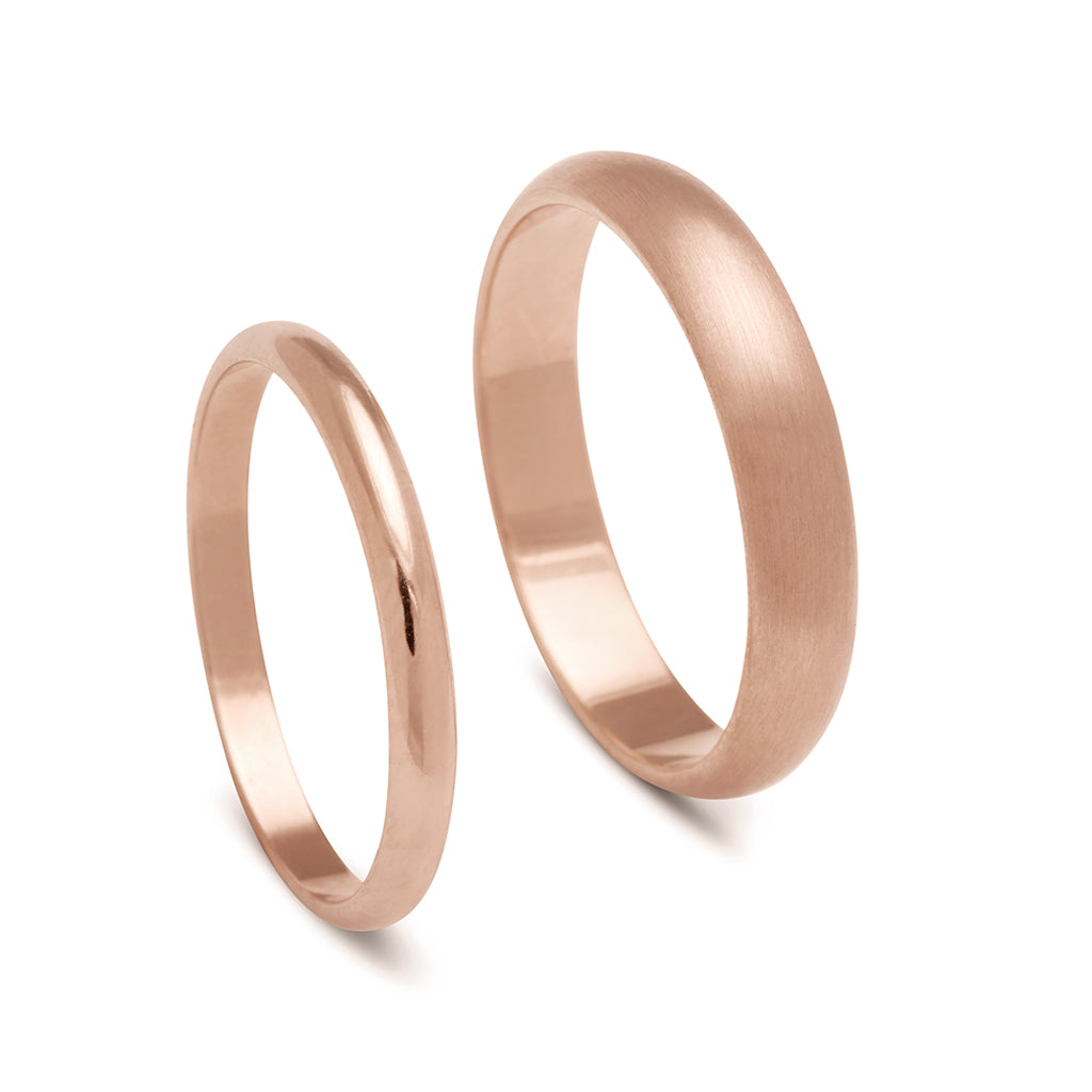 A 2mm classic round band set in rose gold next to a 4mm classic round band with a brushed finish set in rose gold.