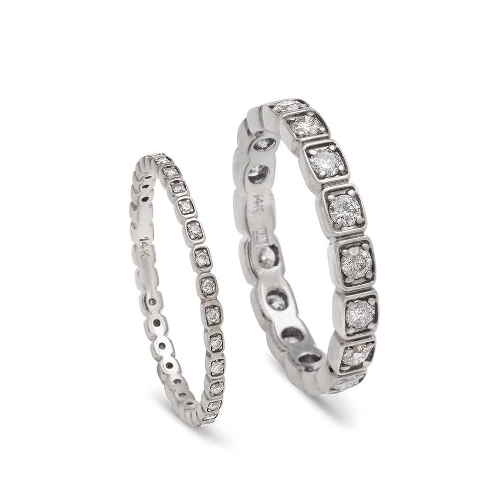 A tiny white diamond eternity band set in white gold next to a 3mm white diamond eternity band set in white gold.