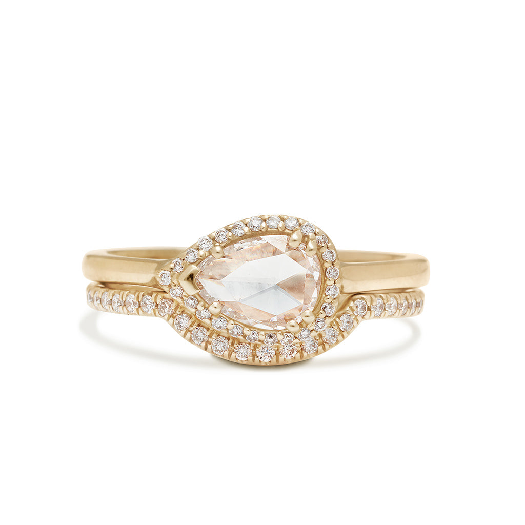 A pear shaped ring with a white diamond and white diamond halo set in yellow gold stacked above a scalloped white diamond yellow gold band.