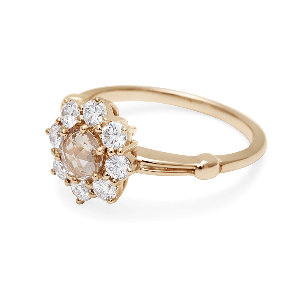 Angled view of a cluster engagement ring with a rose cut champagne diamond center stone and round white diamond stones surrounding it set in yellow gold.