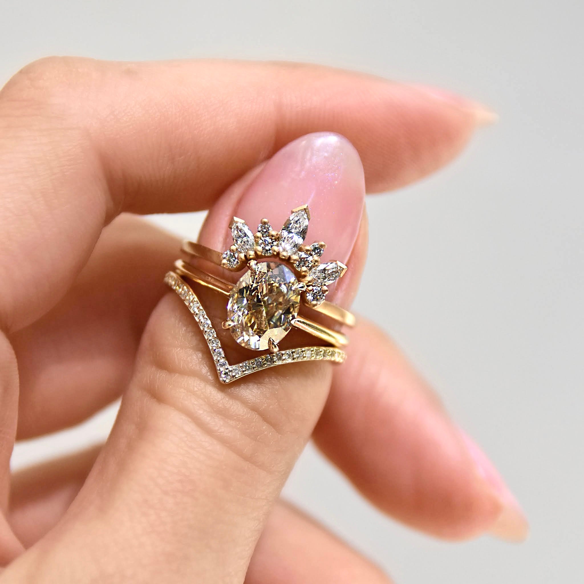 A solitaire ring oval champagne diamond set in yellow gold stacked between two diamond dusted curve bands.