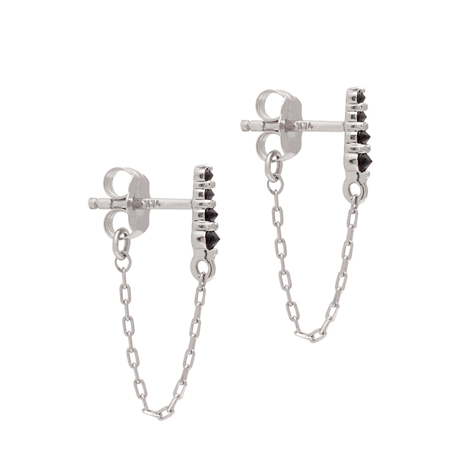 A pair of earrings with four black diamonds with a chain connecting to the ear back set in white gold., White Gold