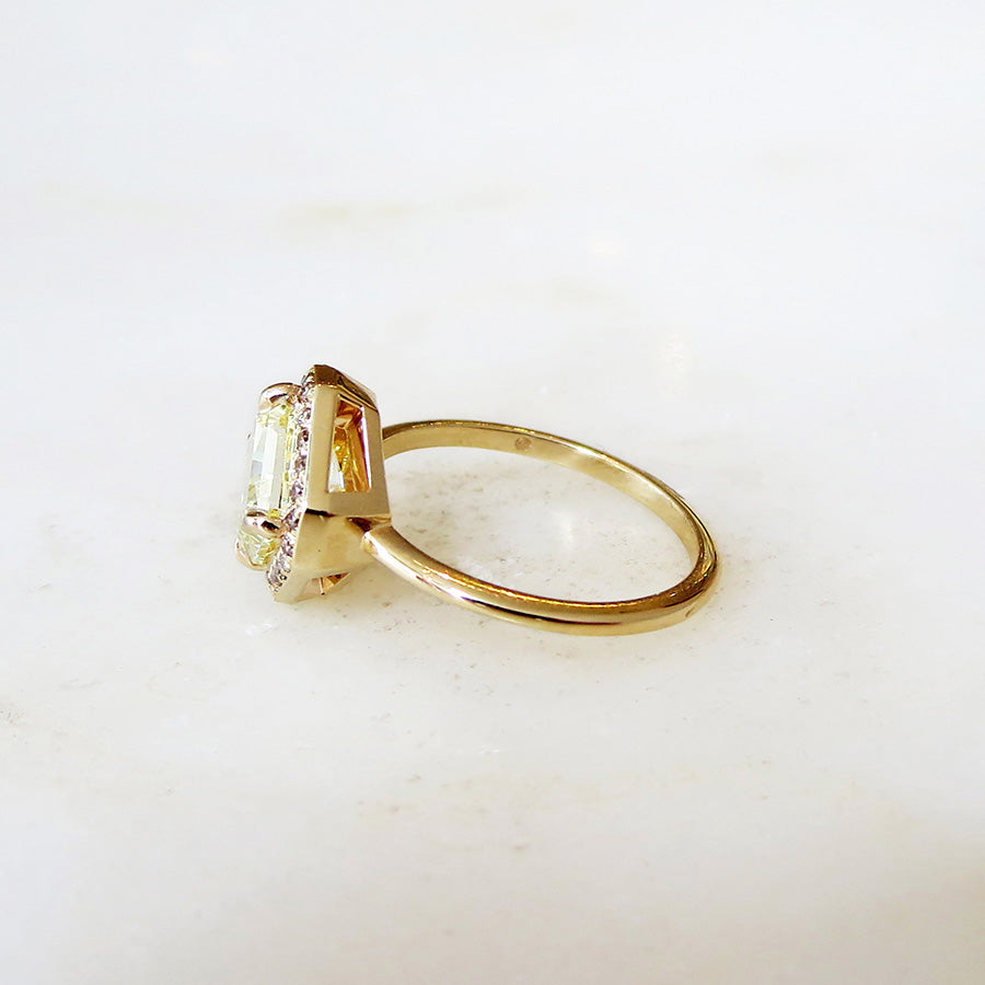 Side view of an engagement ring with a square shape yellow diamond center stone surrounded by a champagne diamond pave halo set in yellow gold on a grey background.