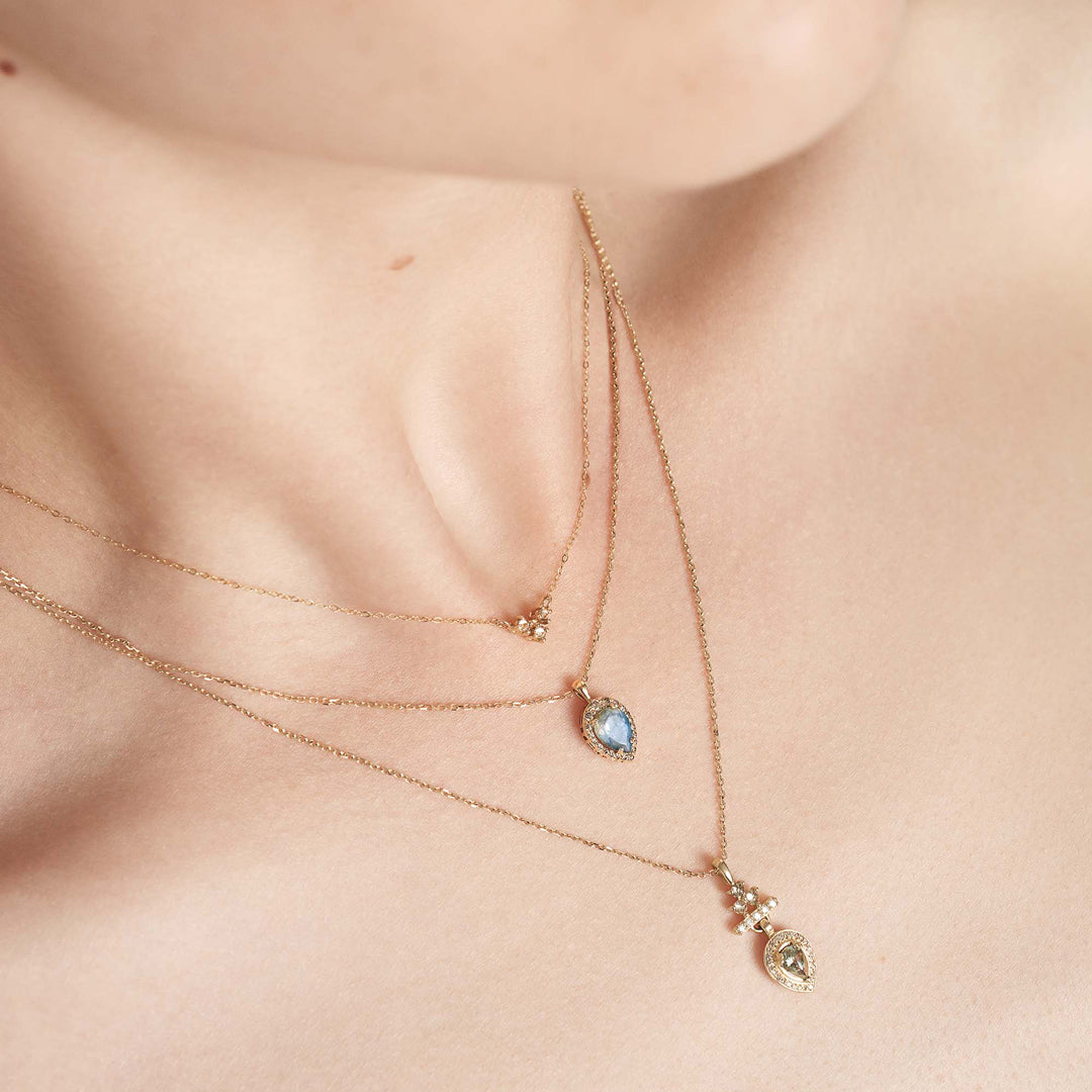 A 16" chain necklace with three black diamonds in the shape of an arrow at the base set in yellow gold stacked above two amulet halo necklaces on a light-complextion models neck.