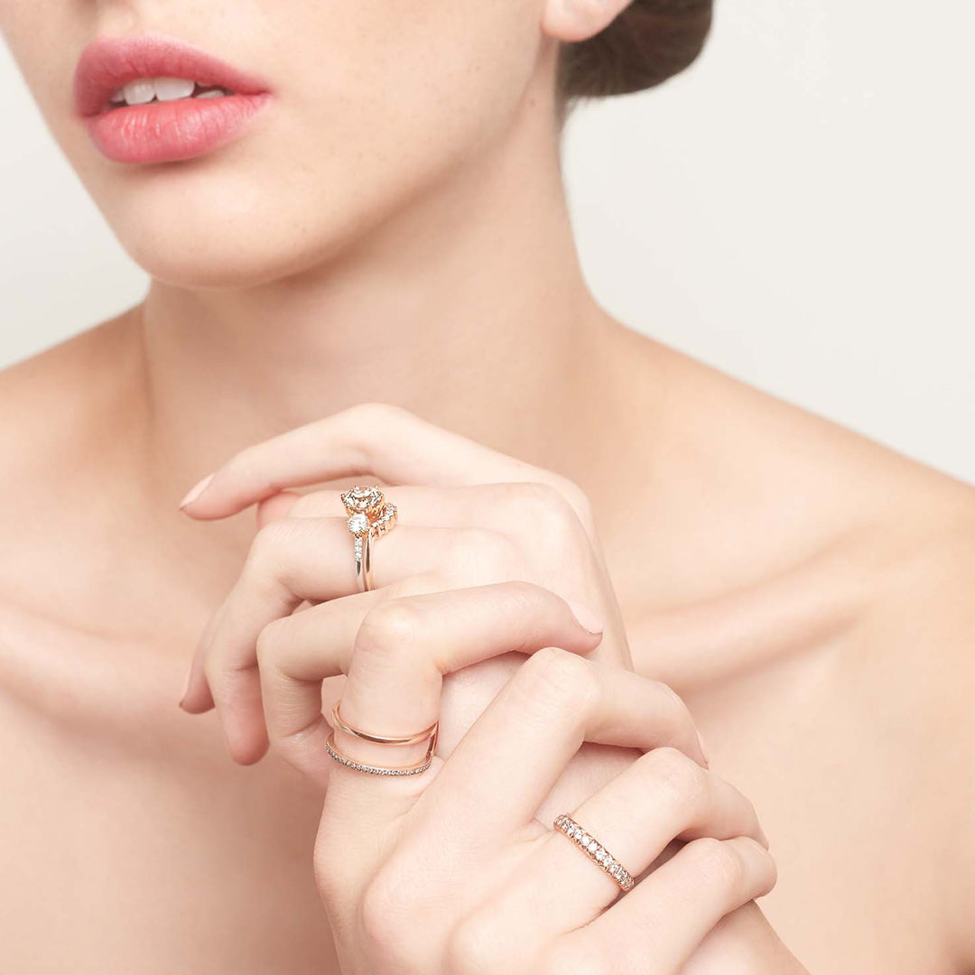 A three stone engagement ring with a round shape white diamond center stone with two white diamond round side stones set in yellow gold stacked above a 7 diamond curve band on a lighter-complextion left hand ring finger.