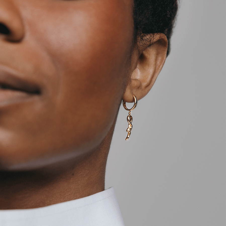 A hoop with a serpent attached set in yellow gold on a dark-complexion model's ear.