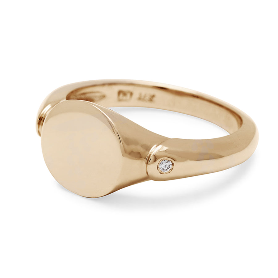Angled view of a solid gold signet ring with two white diamond accents on either side and set in yellow gold.