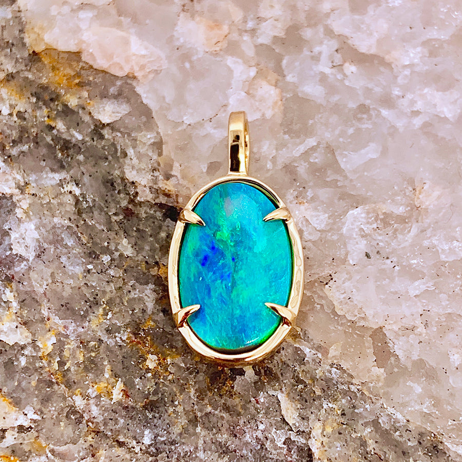 An oval one of a kind turquoise charm in yellow gold chain on a stone.