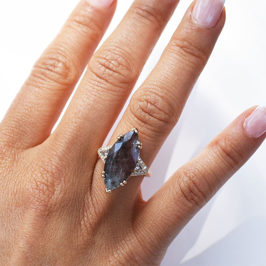 A marquise shaped ring with a quartz center stone with white diamond trillions with white diamond pave halo around them and set in yellow gold on a medium-complextion ring finger