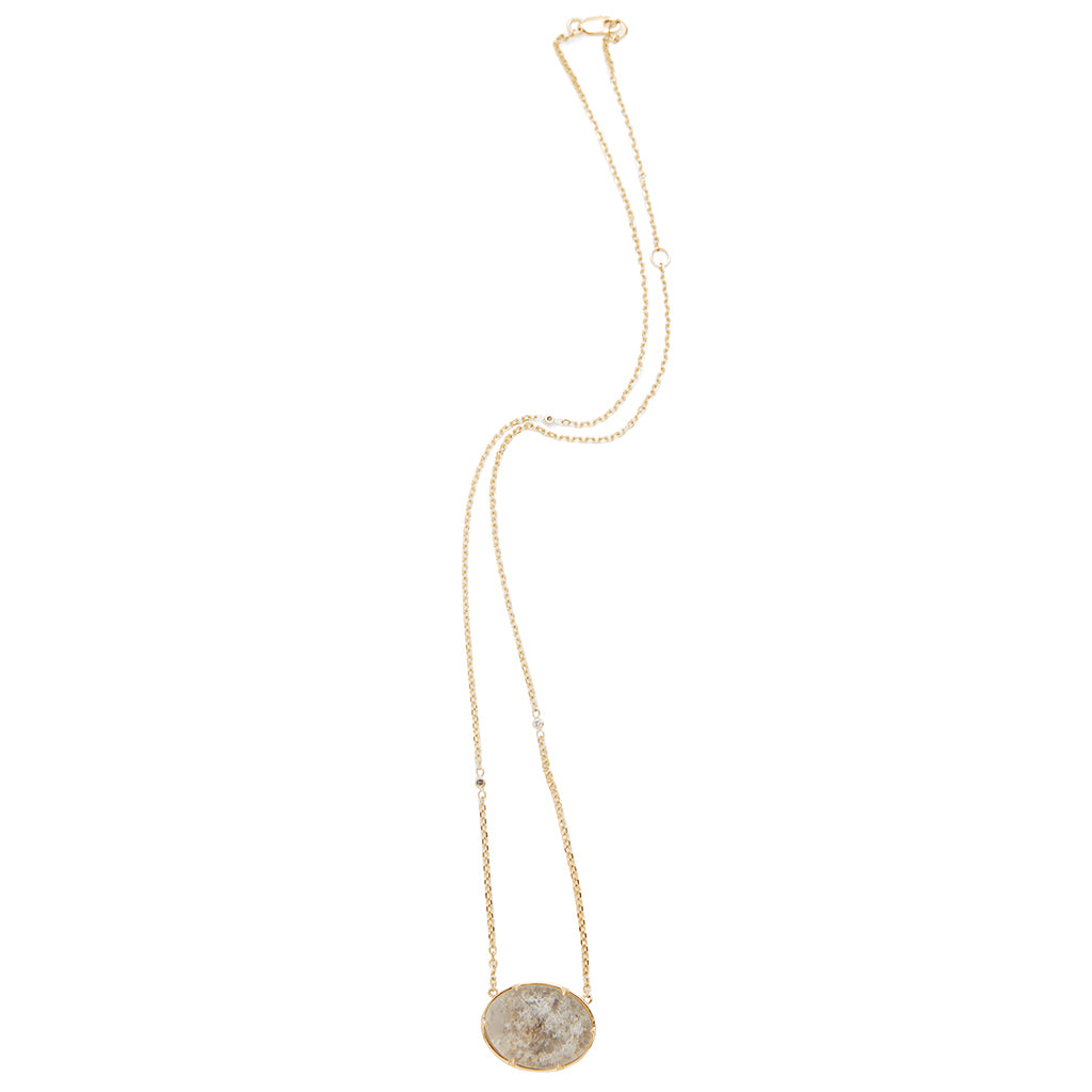 Zoomed out view of an oval quartz charm with a desert like scene in a bezel setting with claw prongs set in yellow gold on a yellow gold chain with grey diamonds on it.