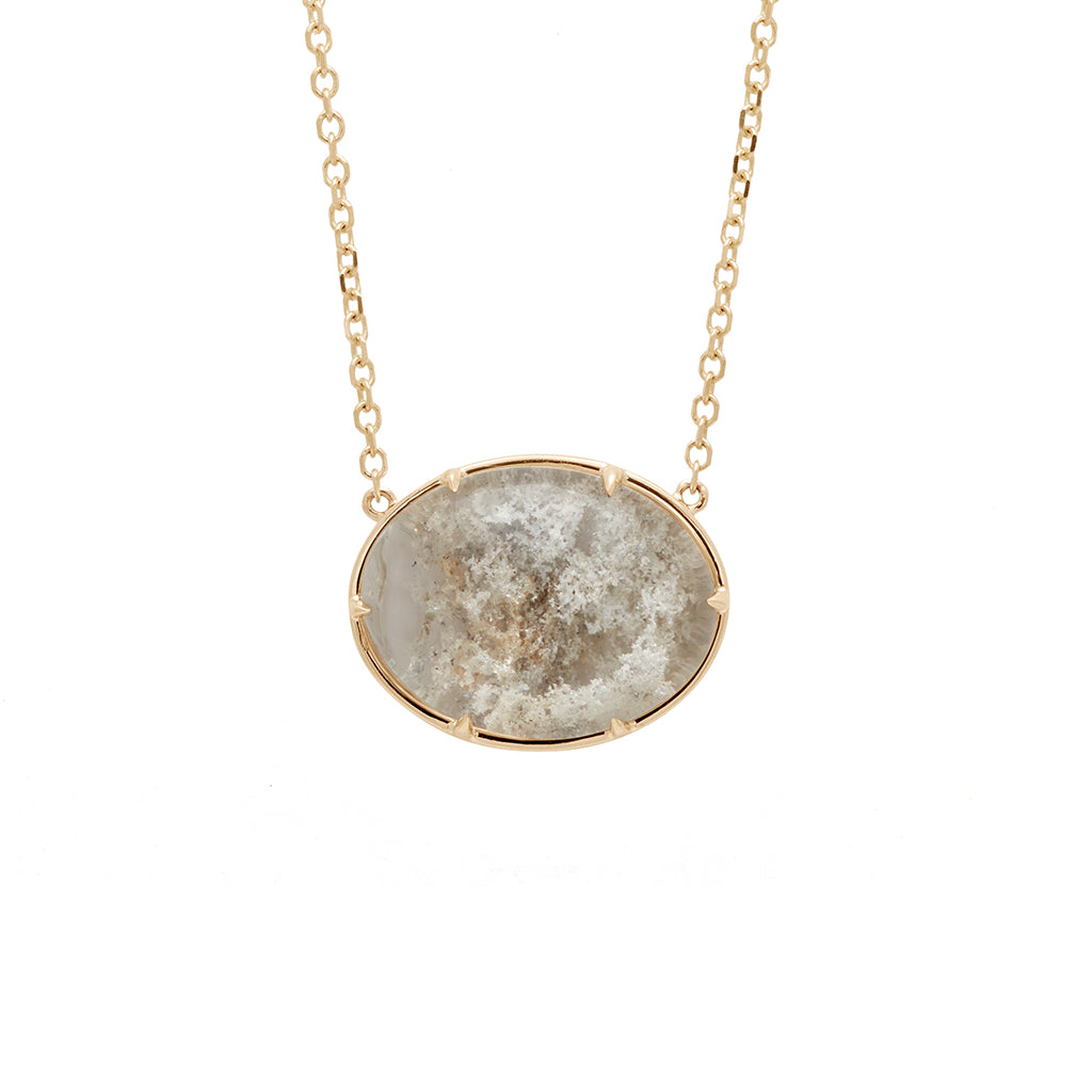 Zoomed in view of an oval quartz charm with a desert like scene in a bezel setting with claw prongs set in yellow gold on a yellow gold chain with grey diamonds on it.