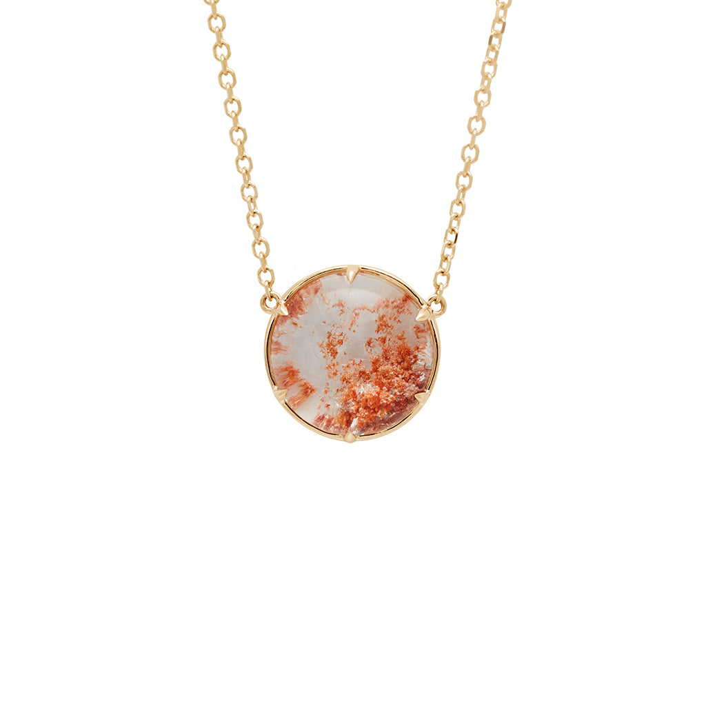 Zoomed in view of a round quartz charm with a desert like scene in a bezel setting with claw prongs set in yellow gold on a yellow gold chain with a champagne diamond on it.