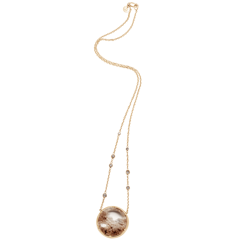 Zoomed out view of a quartz charm with a desert like scene in a bezel setting with claw prongs set in yellow gold on a yellow gold chain with grey diamonds on it.