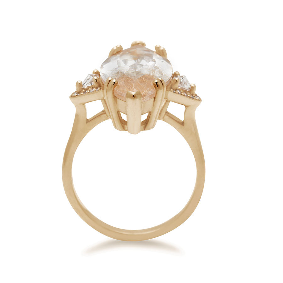 Side view of a three stone engagement ring with a marquise shape copper rutilated quartz center stone with two white diamond trillion side stones with white diamond pave halos around them set in yellow gold.