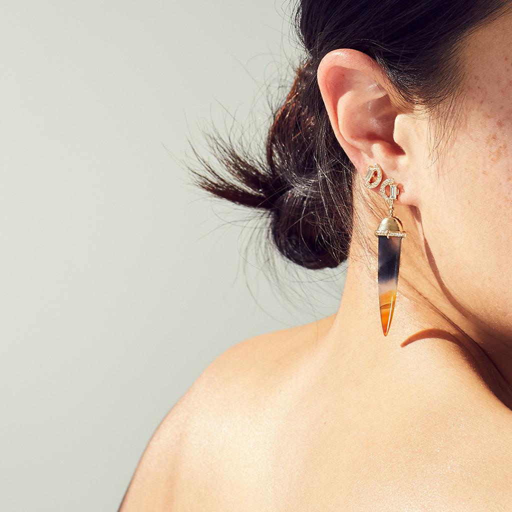 A single chalcedony drop earring with a white diamond arc stud at the top set in yellow gold on a light-complexion model's ear.