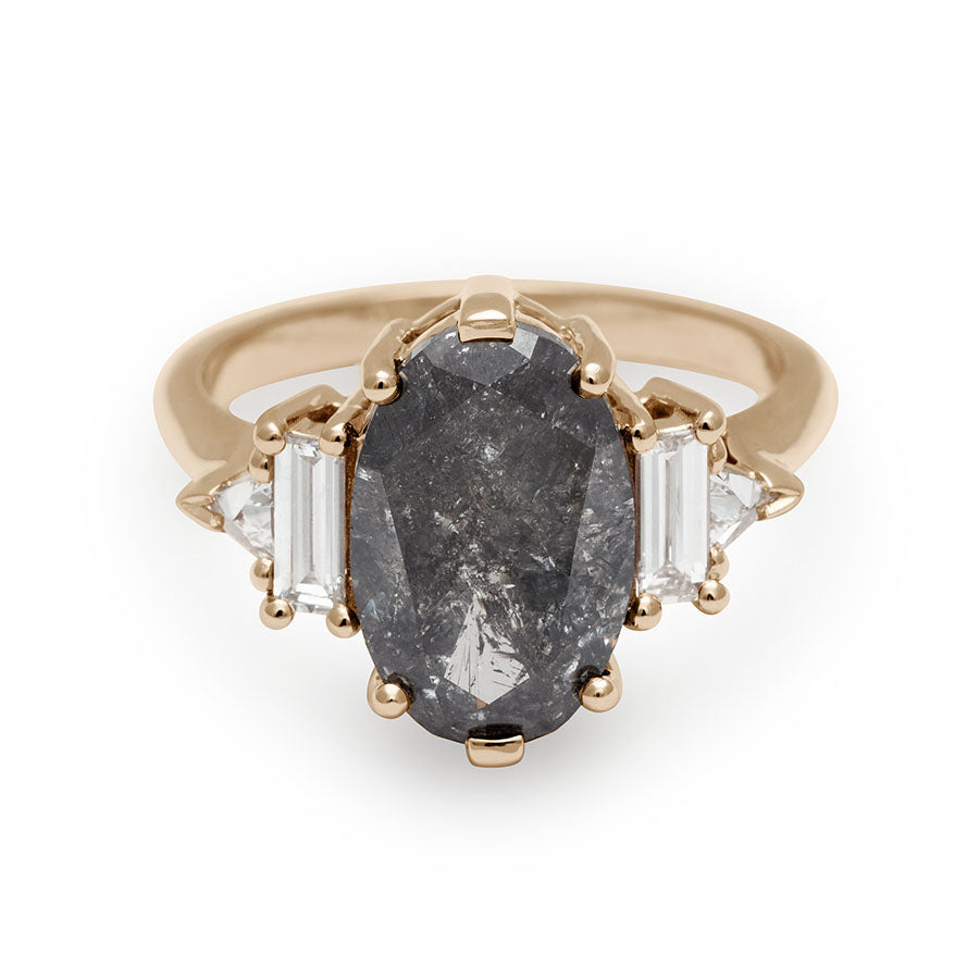 A ring with an oval shaped painted black diamond center stone with one baguette white diamond and one white diamond trillion on either side set in yellow gold.