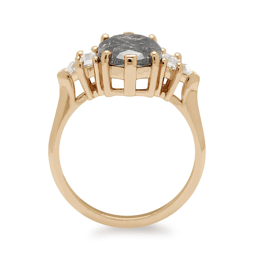 Side view of a ring with an oval shaped painted black diamond center stone with one baguette white diamond and one white diamond trillion on either side set in yellow gold.