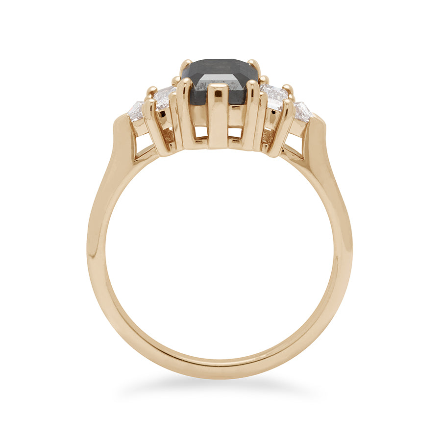 Side view of a ring with an emerald shaped black diamond center stone with one white diamond baguette and one white diamond trillion on either side set in yellow gold.
