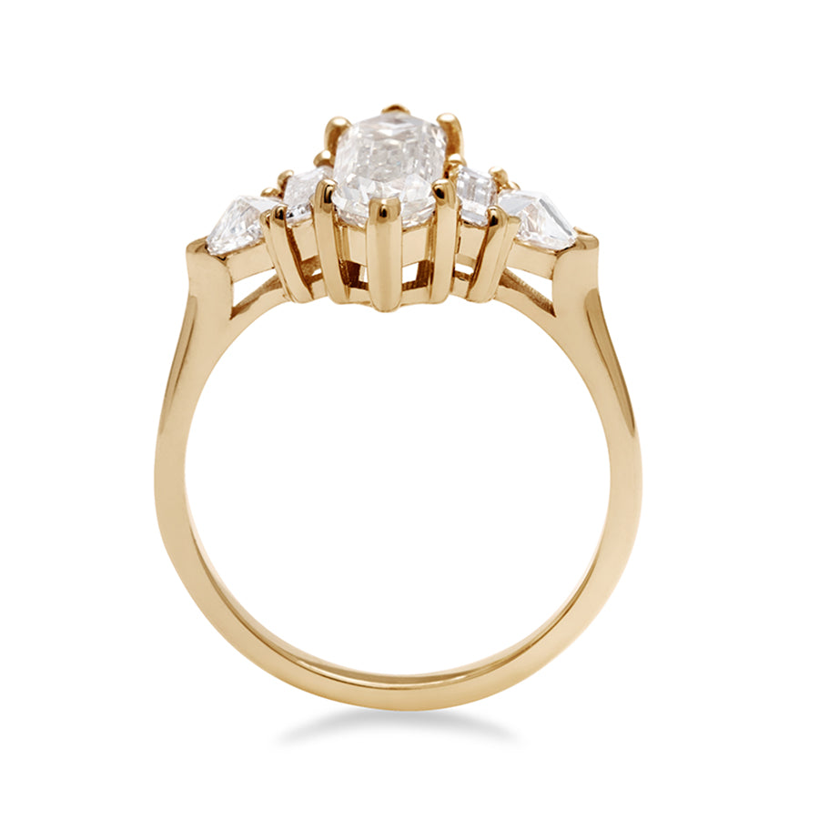Side view of a ring with a hexagonal shaped white diamond center stone with one baguette white diamond and one white diamond trillion on either side set in yellow gold.