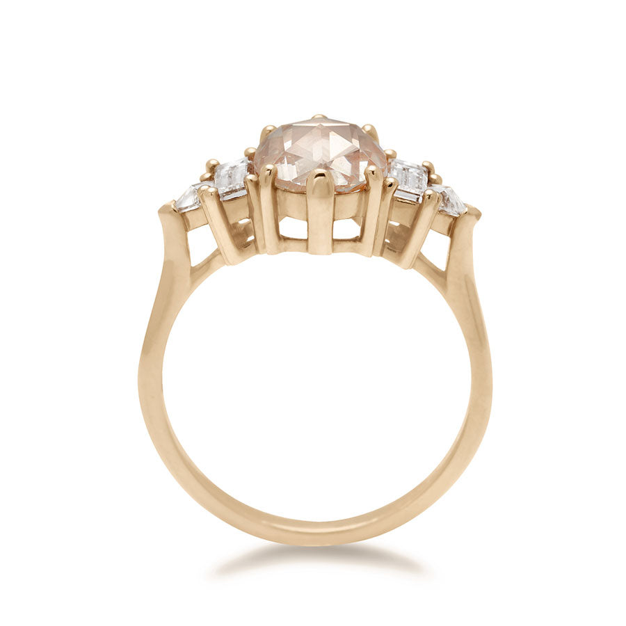 Side view of a ring with a rose cut and oval shaped champagne diamond center stone with one baguette white diamond and one white diamond trillion on either side set in yellow gold.