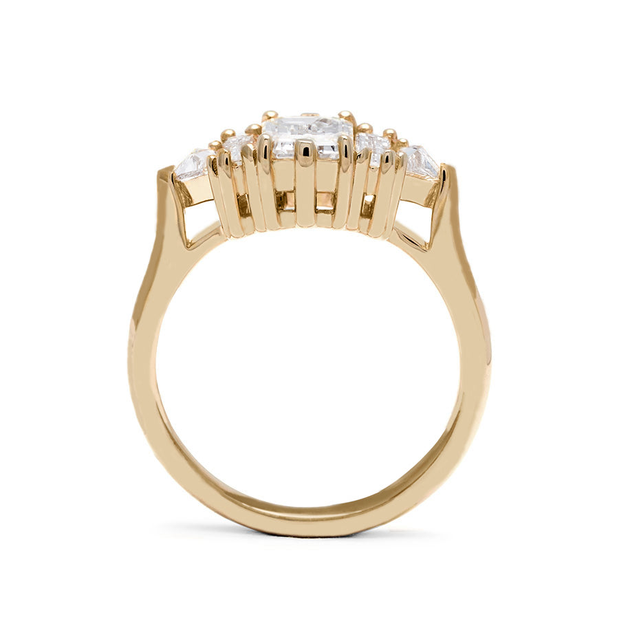 Side view of a ring with an emerald cut and shaped 1.00ct white diamond center stone with one baguette white diamond and one white diamond trillion on either side set in yellow gold.