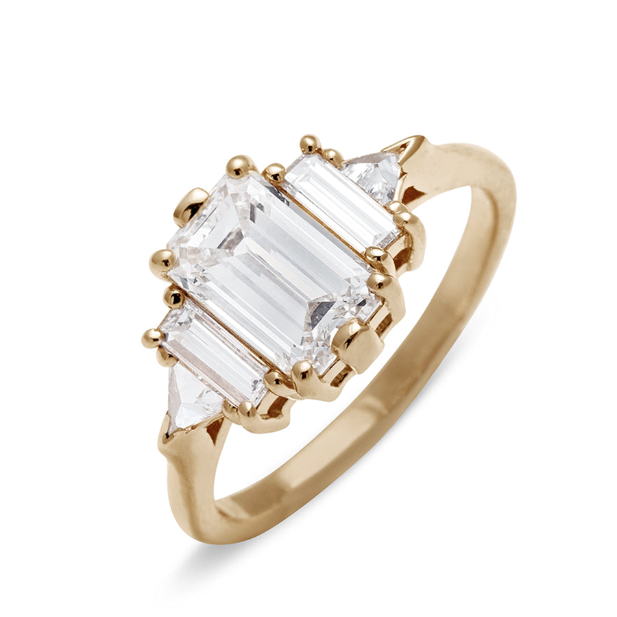 Angled view of a ring with an emerald cut and shaped 1.50ct white diamond center stone with one baguette white diamond and one white diamond trillion on either side set in yellow gold., Yellow Gold