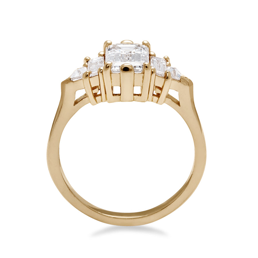 Side view of a ring with an emerald cut and shaped 1.50ct white diamond center stone with one baguette white diamond and one white diamond trillion on either side set in yellow gold.