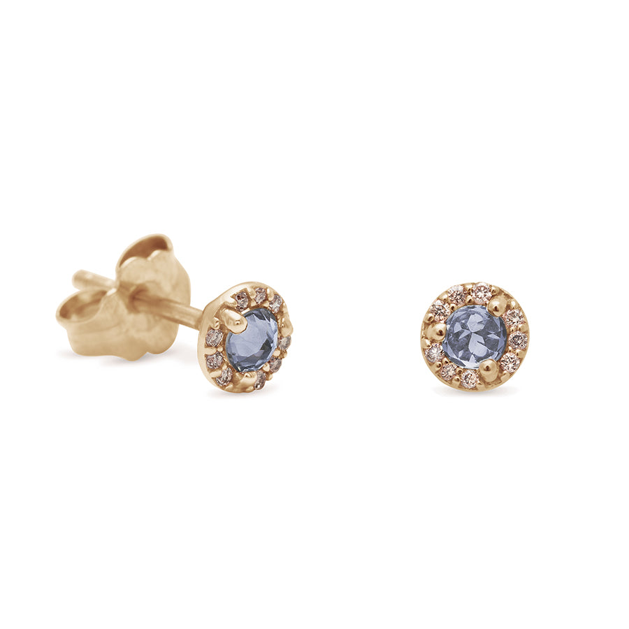 A pair of tiny grey spinel center stone earrings with a halo of white diamond set in yellow gold one earring angled.