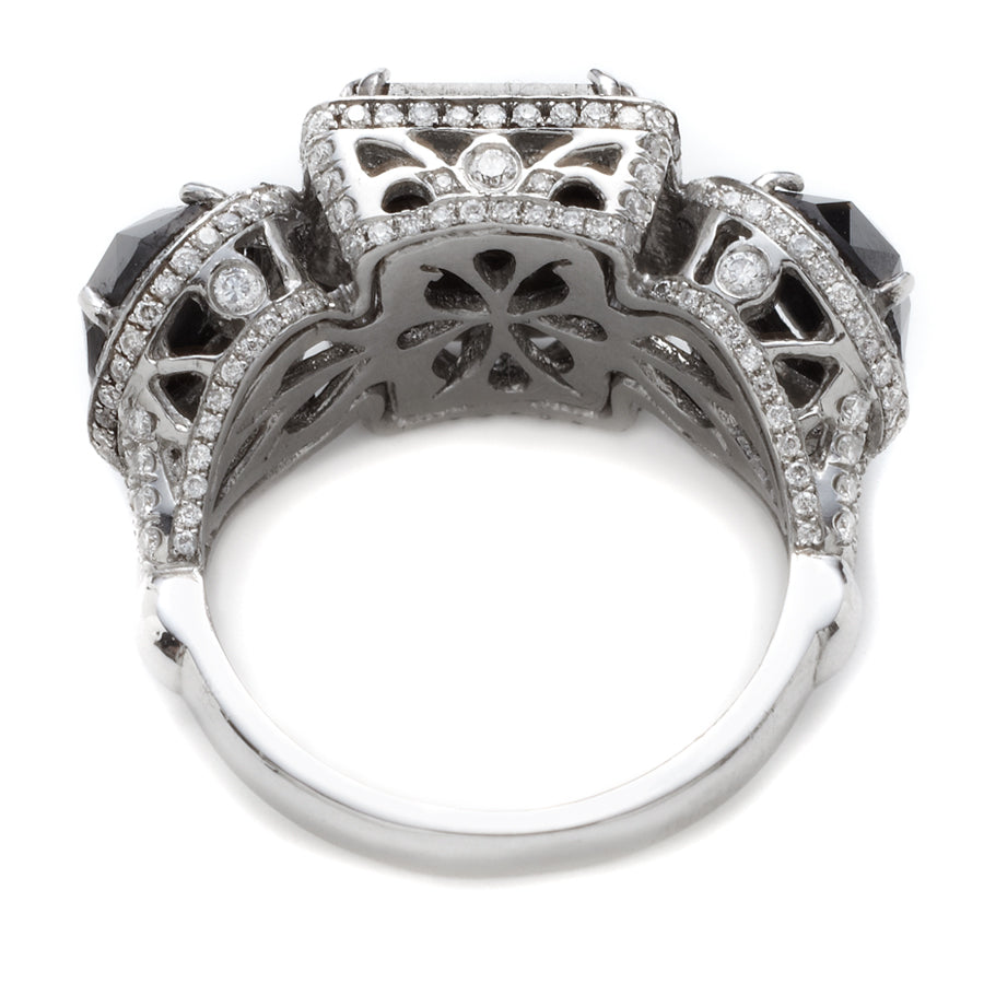 Upside down view of a three stone ring with an emerald cut and emerald shape black diamond center stone with two round black diamond side stones. All surrounded with white diamond pave halo set in platinum.