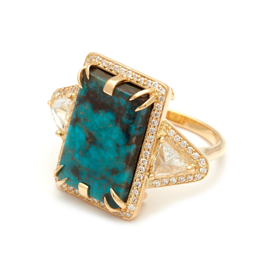 Angled view of an emerald shaped turquoise set between two white diamond trillion side stones and all encircled in white diamond pave halo set in yellow gold.
