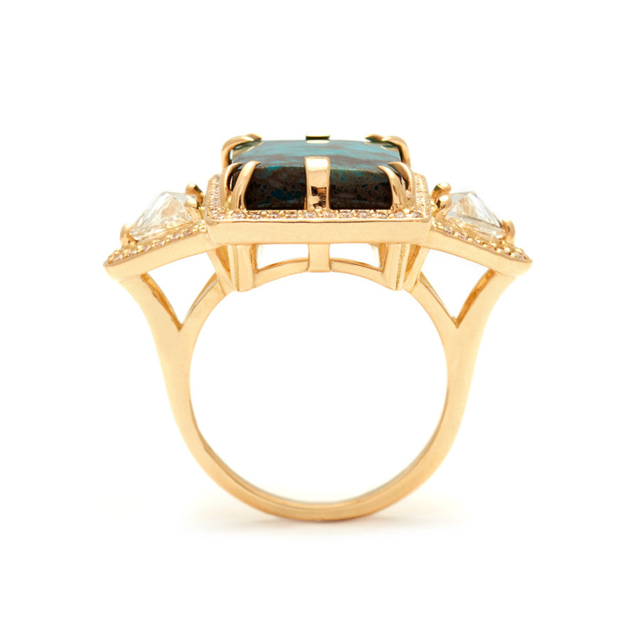 Side view of an emerald shaped turquoise set between two white diamond trillion side stones and all encircled in white diamond pave halo set in yellow gold.