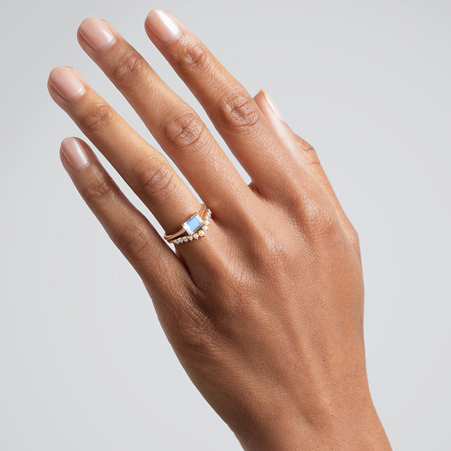 An east/west solitaire ring with an emerald shape rainbow moonstone set in yellow gold above a curved pearl and white dimaond band on a darker complexion hand., White Gold, Rose Gold, Yellow Gold