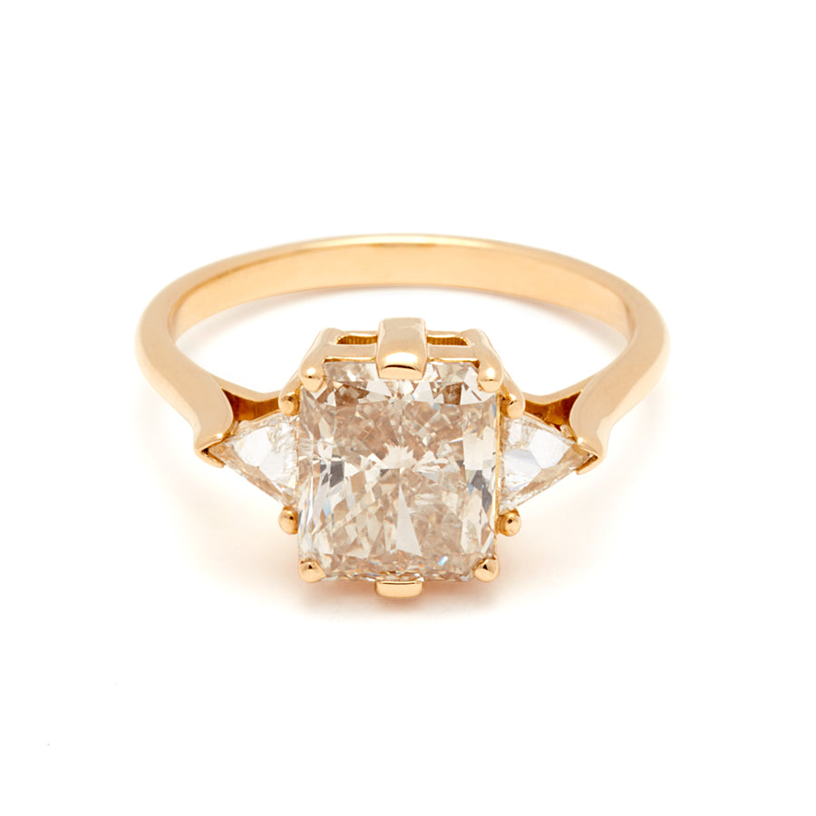 A three stone engagement ring with an emerald shape champagne diamond center stone with two white diamond trillion side stones set in yellow gold.
