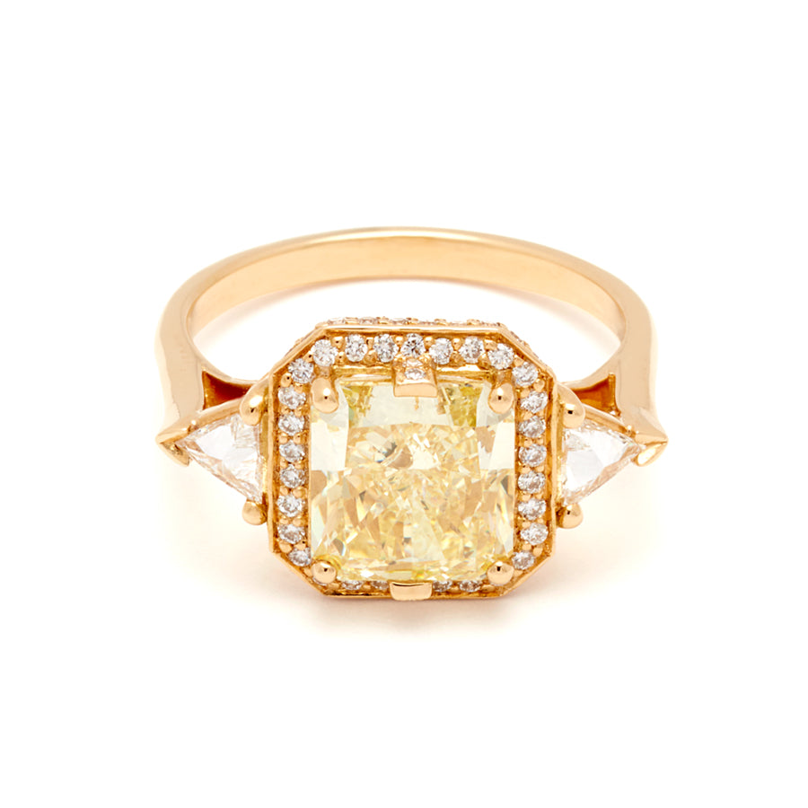 A three stone engagement ring with an radiant cut yellow diamond center stone surrounded by a white diamond pave halo with two white diamond trillion side stones set in yellow gold.