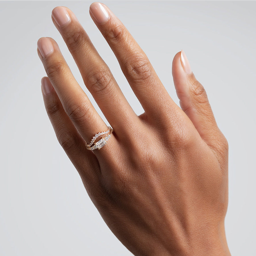 A ring with an emerald cut and shaped white diamond center stone with two round white diamonds on either side set in yellow gold below an 11 round white diamond curve band on a medium complexion model., White Gold, Rose Gold, Yellow Gold
