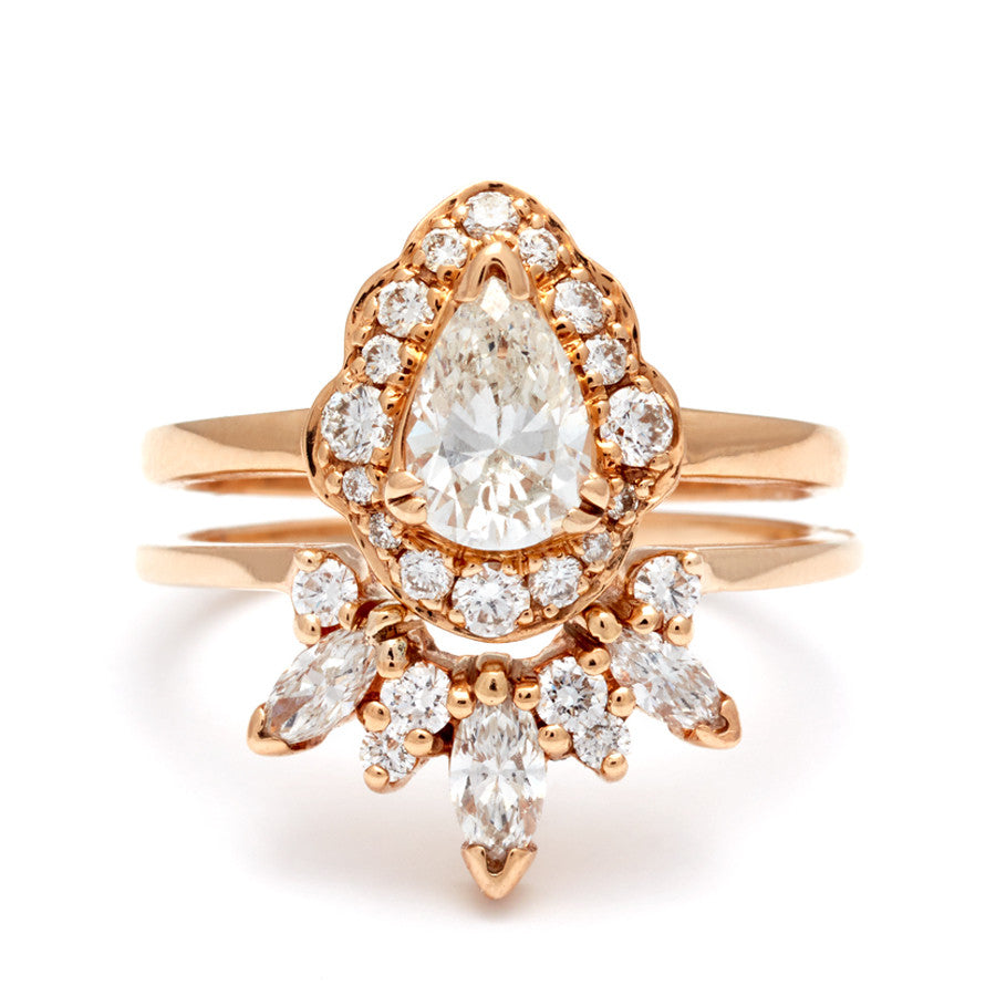 A diamond halo engagement ring with a pear white diamond center stone set in yellow gold stacked above a white diamond marquise nesting band.
