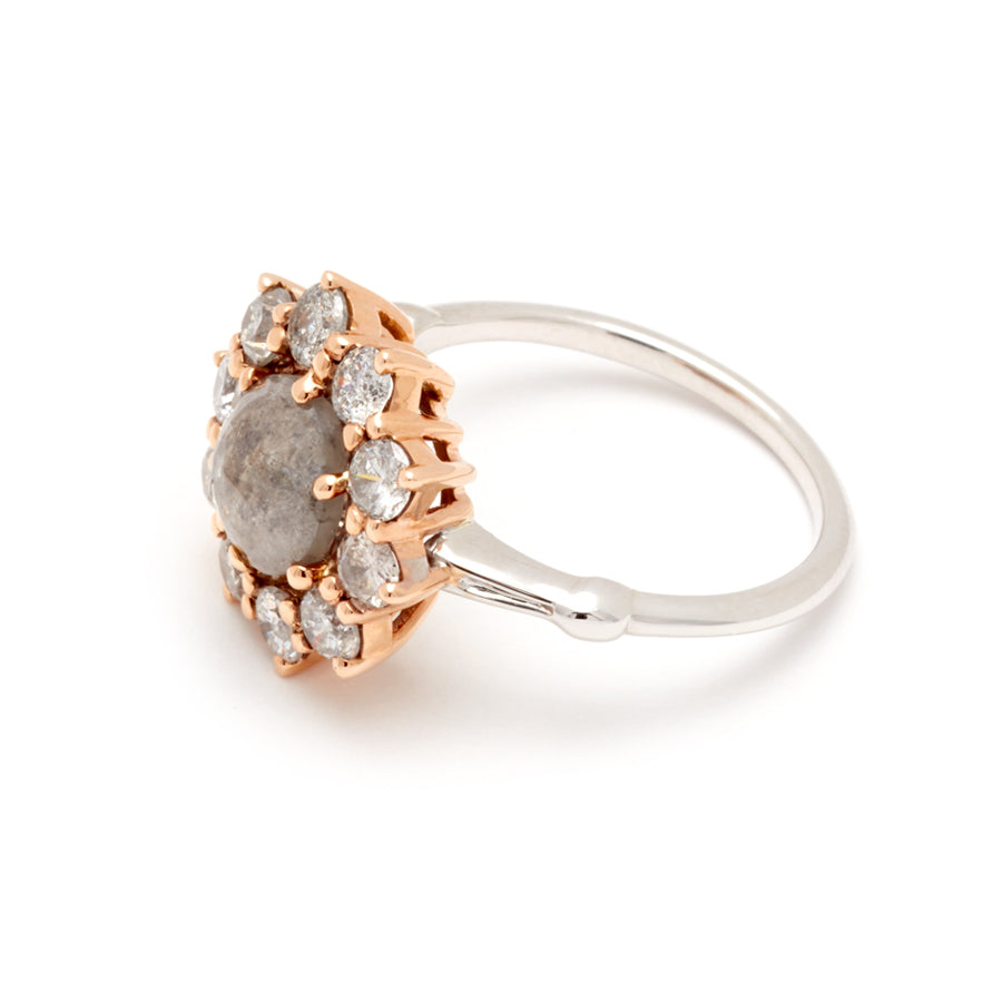 Angled view of a ring with a rose cut grey diamond center stone surrounded by round grey diamonds set in a rose gold basket and white gold band.