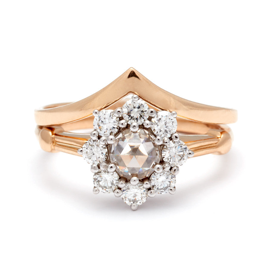 A cluster engagement ring with a rose cut champagne diamond center stone and round white diamond stones surrounding it set in yellow gold stacked beneath a solid gold chevron band.