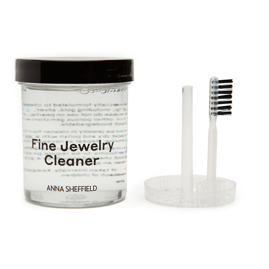 "Anna Sheffield Fine Jewelry Cleaner" in a small jar with clear liquid with a brush on the side.